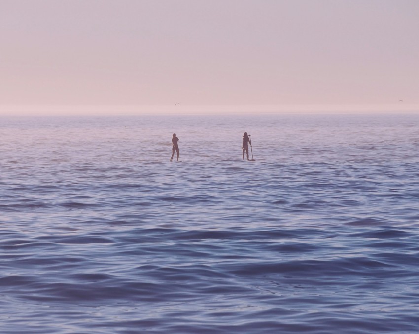 two person standing on surfboard on sea at sunrise