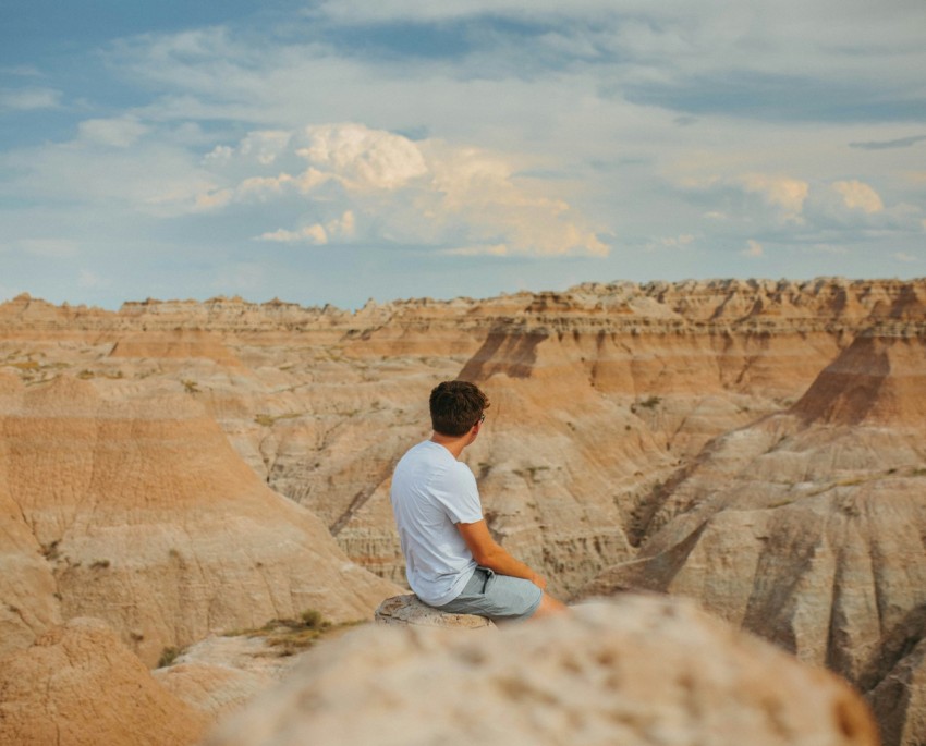 man in white t shirt sitting on brown rock formation during daytime