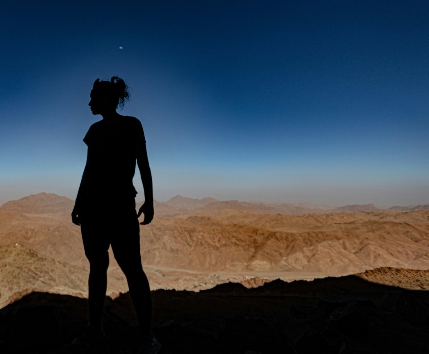 a silhouette of a woman standing on top of a mountain 1r3155k7j