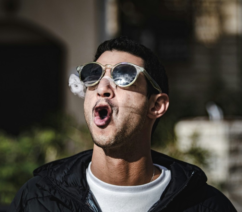 a man with sunglasses blowing out a cigarette