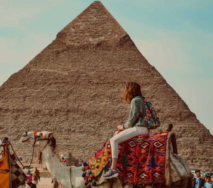 a woman sitting on top of a camel in front of a pyramid hXb5W