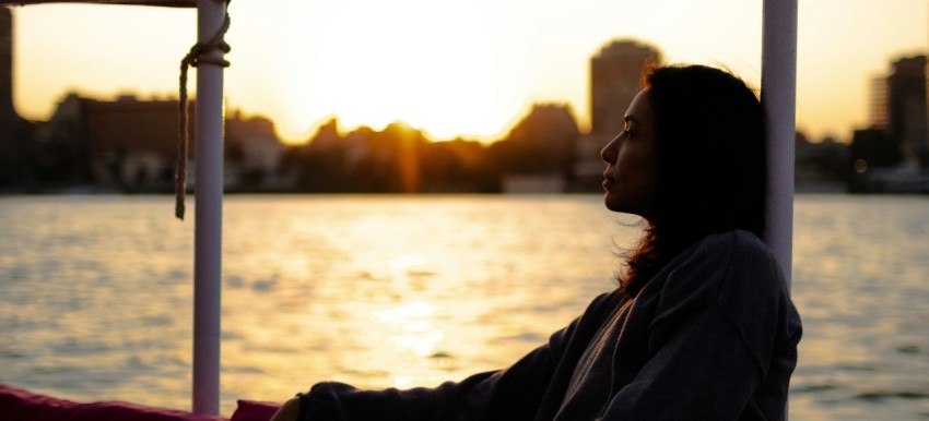 a woman is sitting on a boat at sunset IyIh