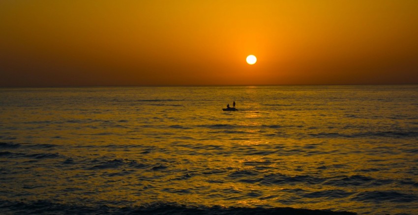 the sun is setting over the ocean with a boat in the water