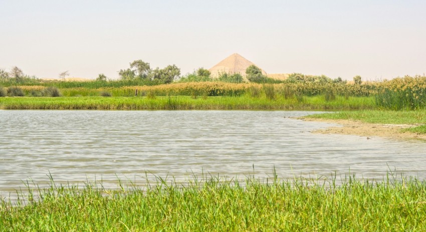 a large body of water surrounded by a lush green field 0b