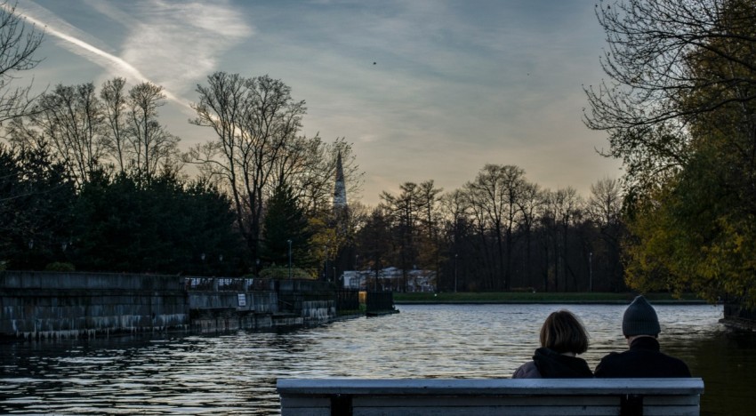 two people sitting on a bench looking at the water