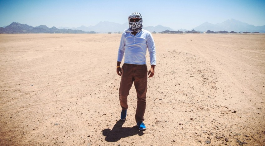 man in white dress shirt and brown pants standing on brown sand during daytime