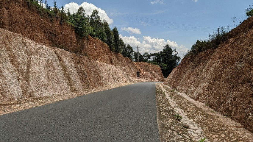 gray asphalt road between brown mountain under blue sky during daytime