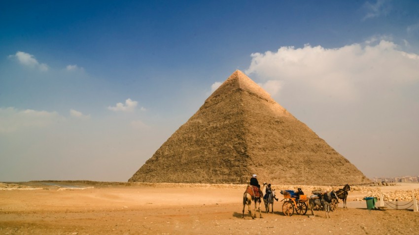 people riding horses on brown sand near pyramid during daytime