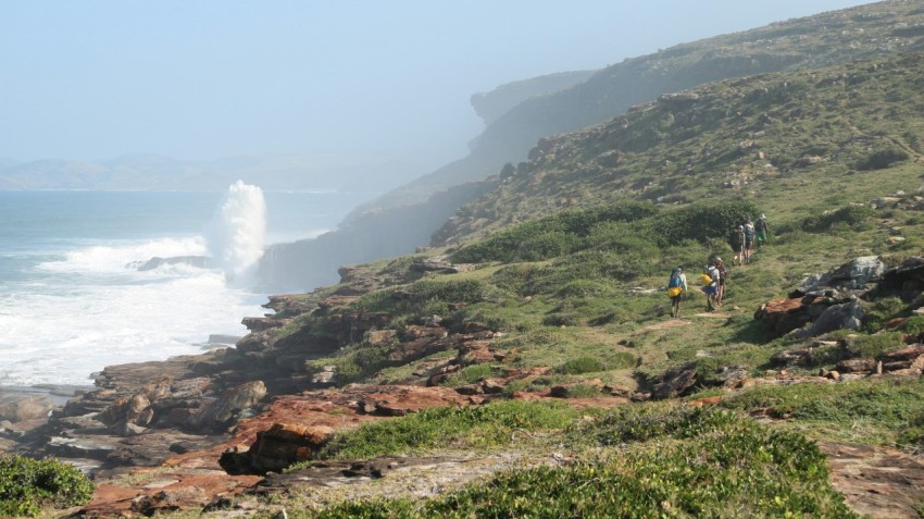 a group of people walking up a hill next to the ocean n2og3g9en