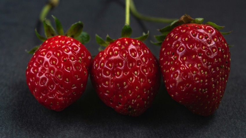 three ripe strawberries on a black surface