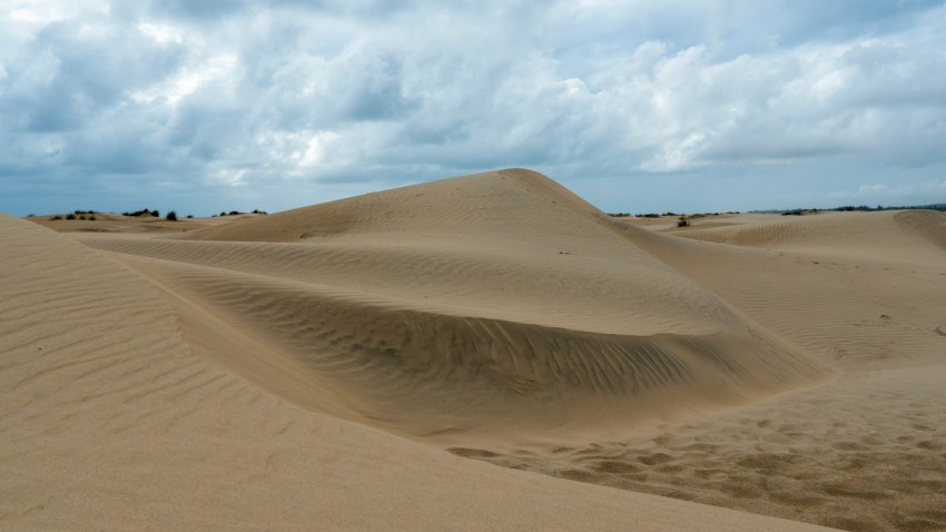 a large sand dune with a few clouds in the sky