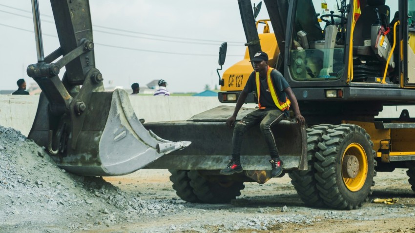 man in yellow and black jacket standing beside black and yellow heavy equipment