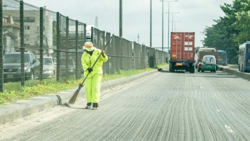 man in green jacket and green pants holding shovel walking on road during daytime