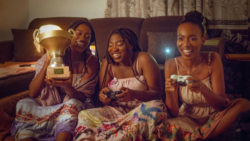 three women sitting on a couch holding remote controls