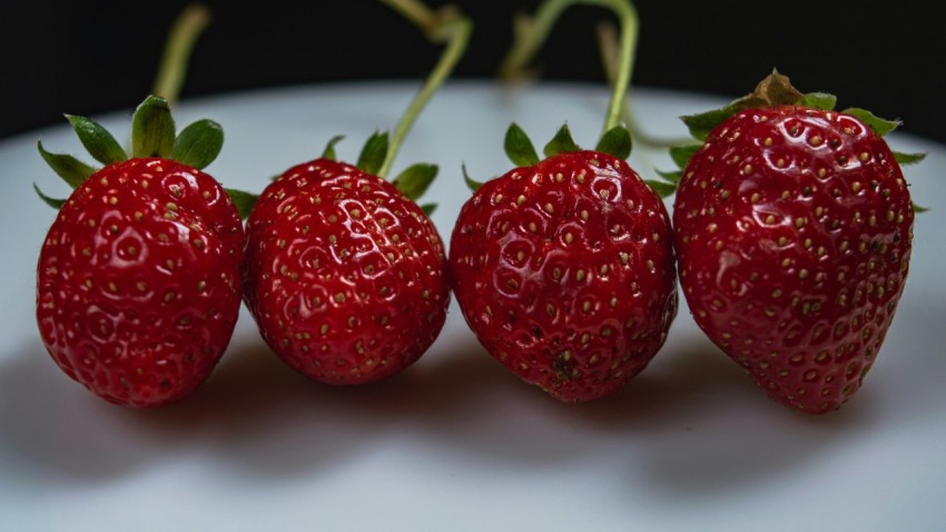 a group of three strawberries sitting on top of a white plate