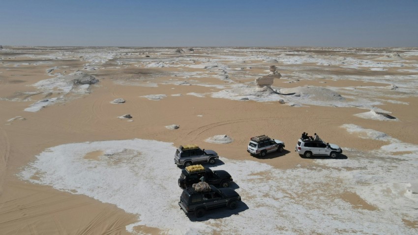 a group of four vehicles driving through a desert 9Etp