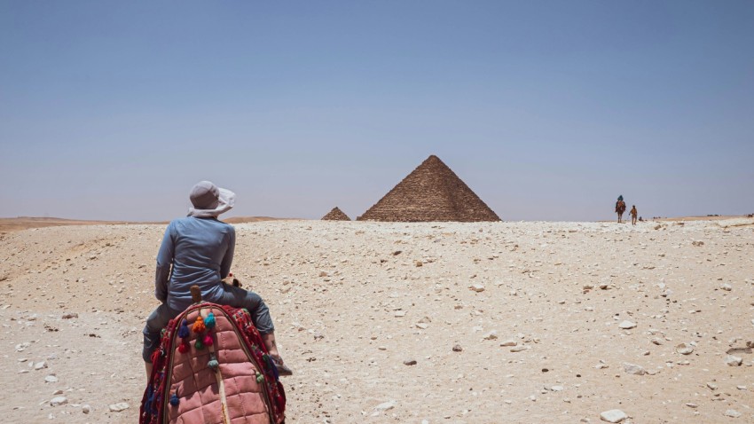 a man sitting on a rock with a pyramid in the background