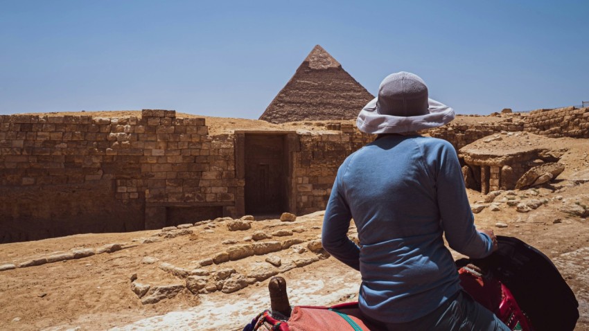 a person sitting on a rock ledge looking at a pyramid