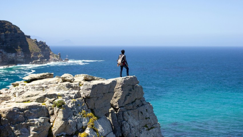 man in black jacket standing on gray rock formation near body of water during daytime