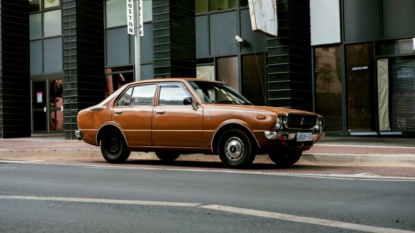 brown sedan parked beside gray concrete building during daytime