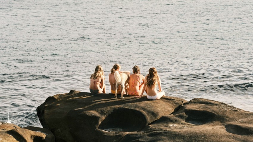 a group of women sitting on top of a rock next to the ocean