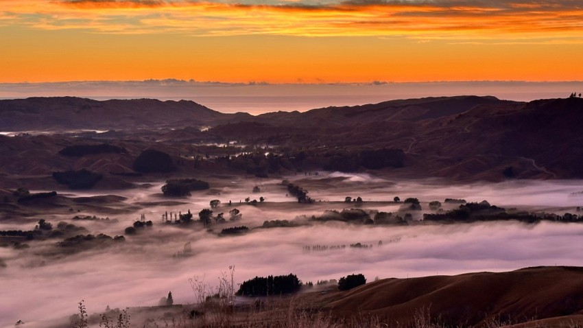 a view of a valley covered in fog at sunset