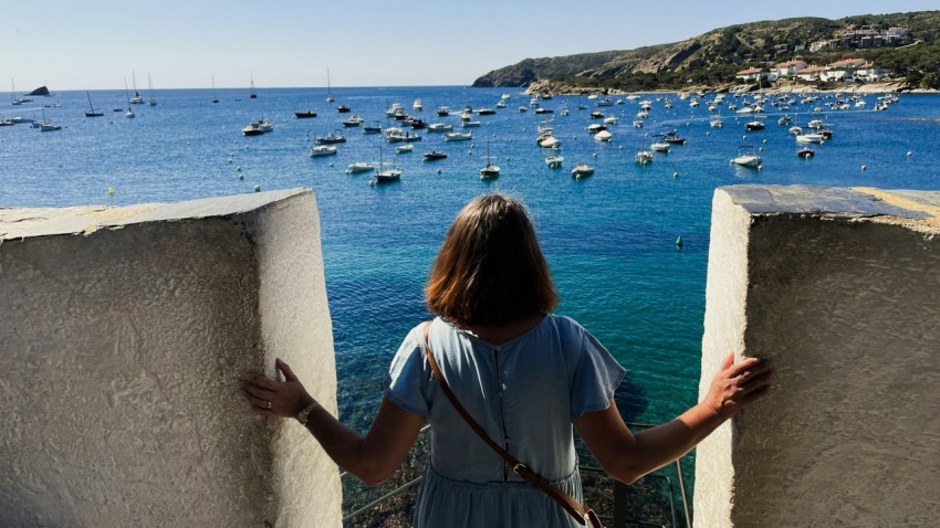 a woman standing on a ledge looking at boats in the water