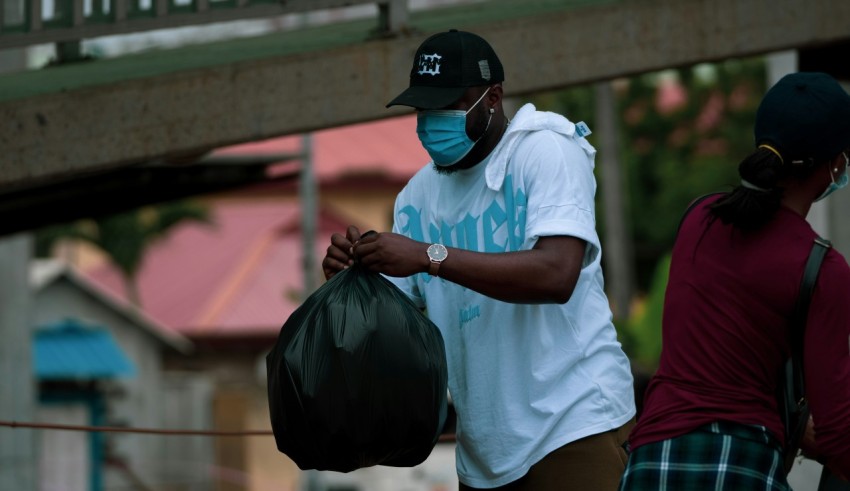 man in white polo shirt and black cap holding black plastic bag