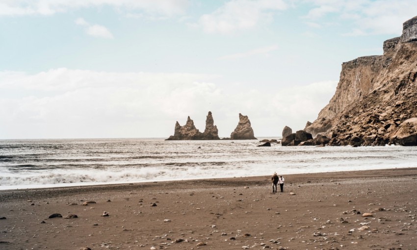 two person walking on seashore under clear blue sky