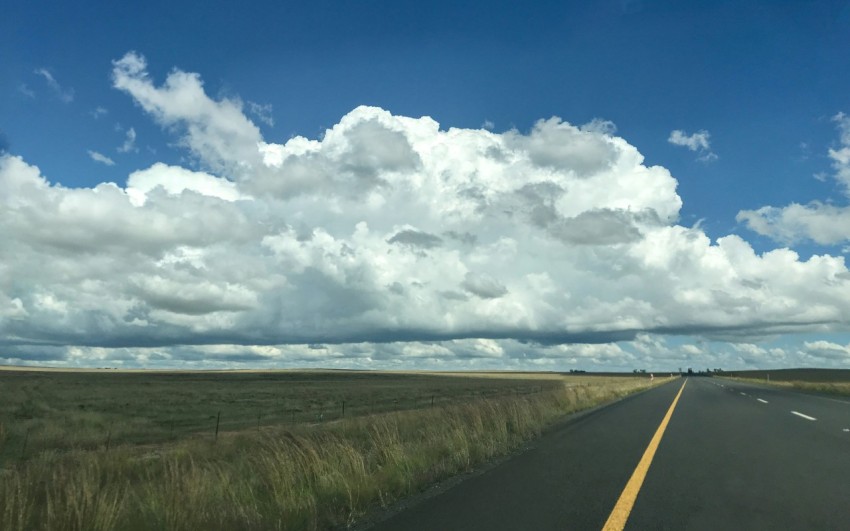 gray concrete road between green grass under white clouds and blue sky during daytime