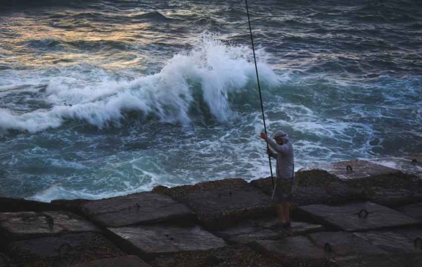 a man holding a fishing pole next to a body of water