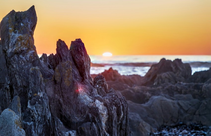 the sun is setting over a rocky beach