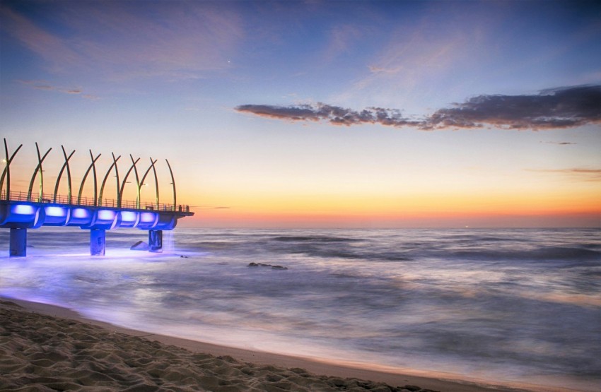 a pier on the beach at sunset with blue lights