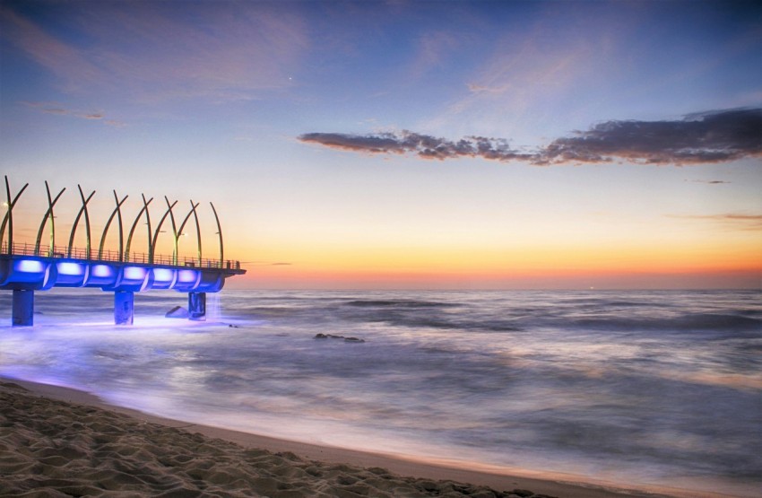 a pier on the beach at sunset with blue lights