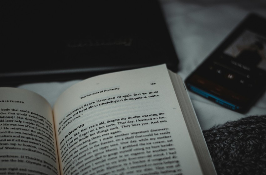 an open book sitting on top of a bed next to a cell phone