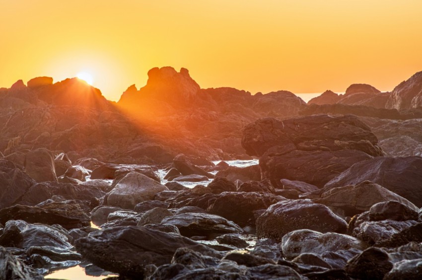 the sun is setting over a rocky beach kbNrUnWu