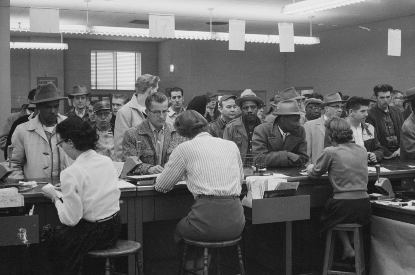 unemployed men including african americans line up at a counter for assistance from women office workers at an unemployment office detroit michigan