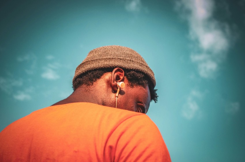 man in orange crew neck shirt wearing brown knit cap and silver framed eyeglasses under blue