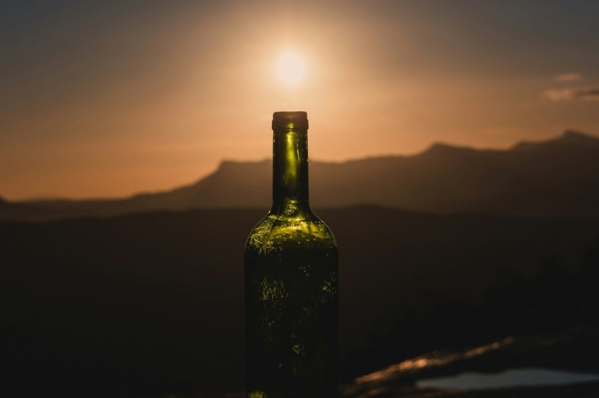 green glass bottle on brown wooden table during sunset E_To