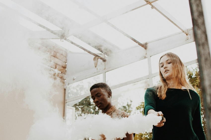 woman holding device emitting smoke beside man