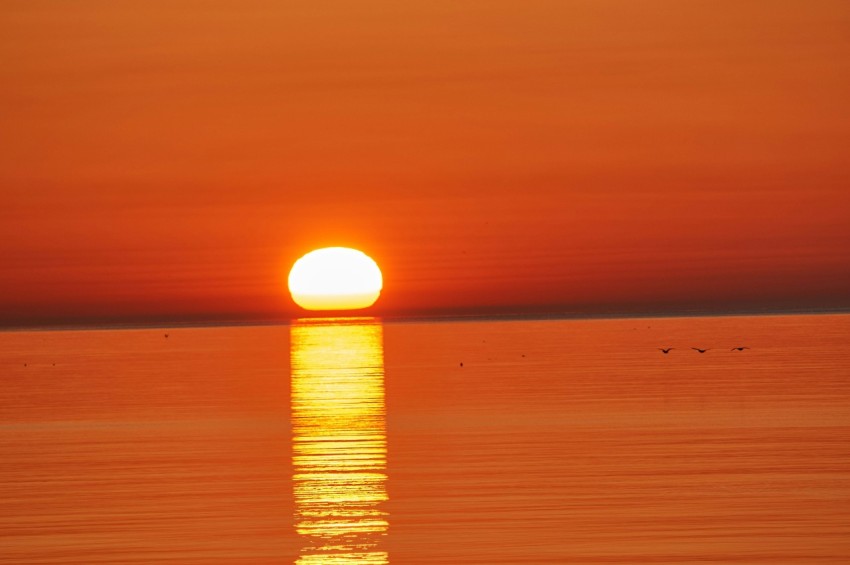 the sun is setting over the ocean with a boat in the water