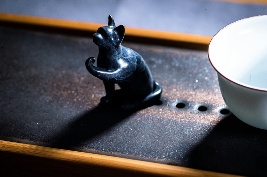 a black cat figurine next to a white bowl