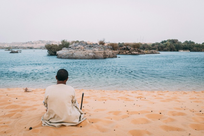 man sits on sand dunes while watching the beach