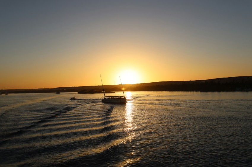 a boat traveling across a body of water at sunset