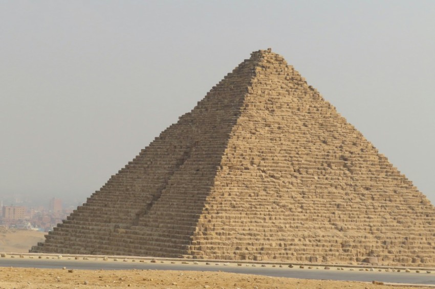 a giraffe standing in front of a very tall pyramid