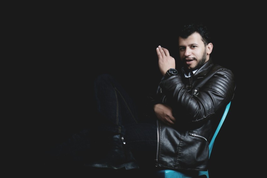 a man in a leather jacket sitting on a chair FeKc