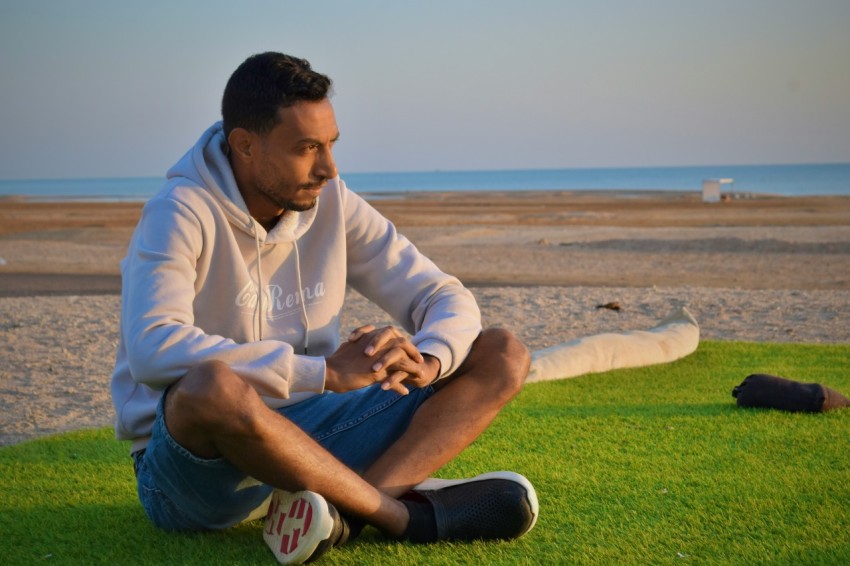 a man sitting on the grass on the beach