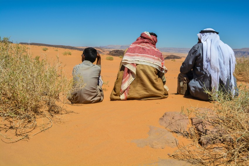 a couple of people sitting on top of a sandy field