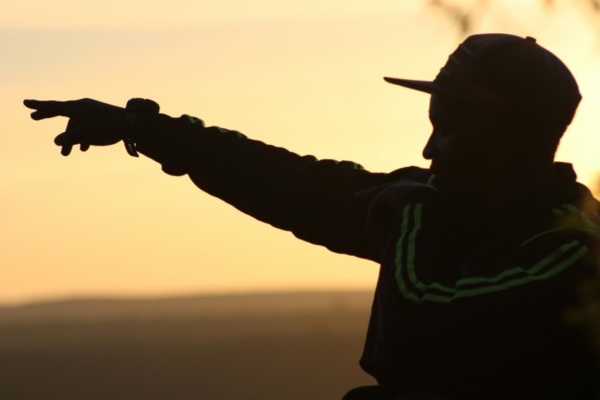 a silhouette of a man pointing at the sun