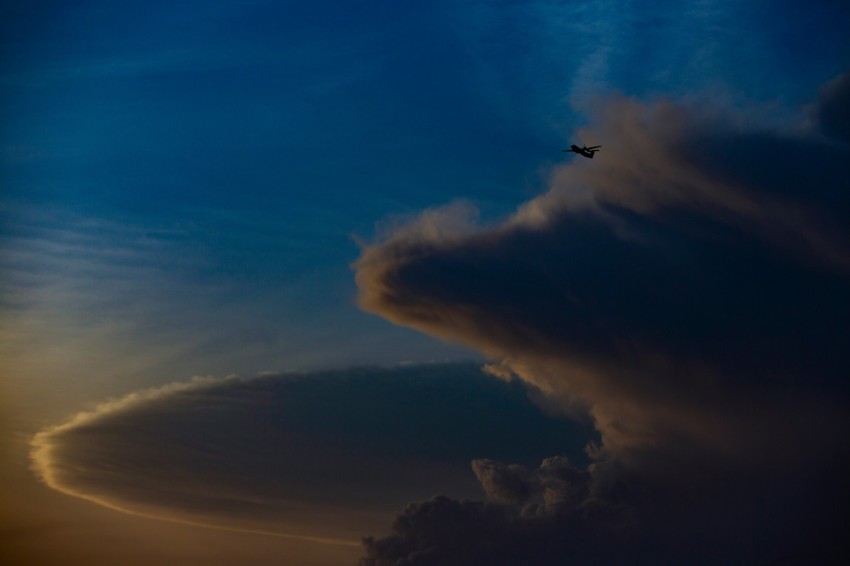 a plane flying through a cloudy sky at sunset